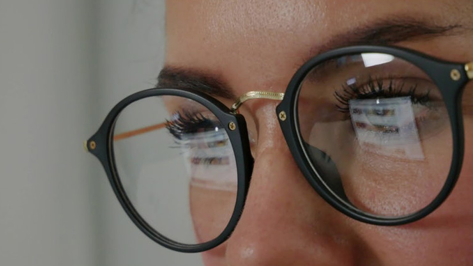 Close-up of a man's face wearing glasses that are reflecting his screen.
